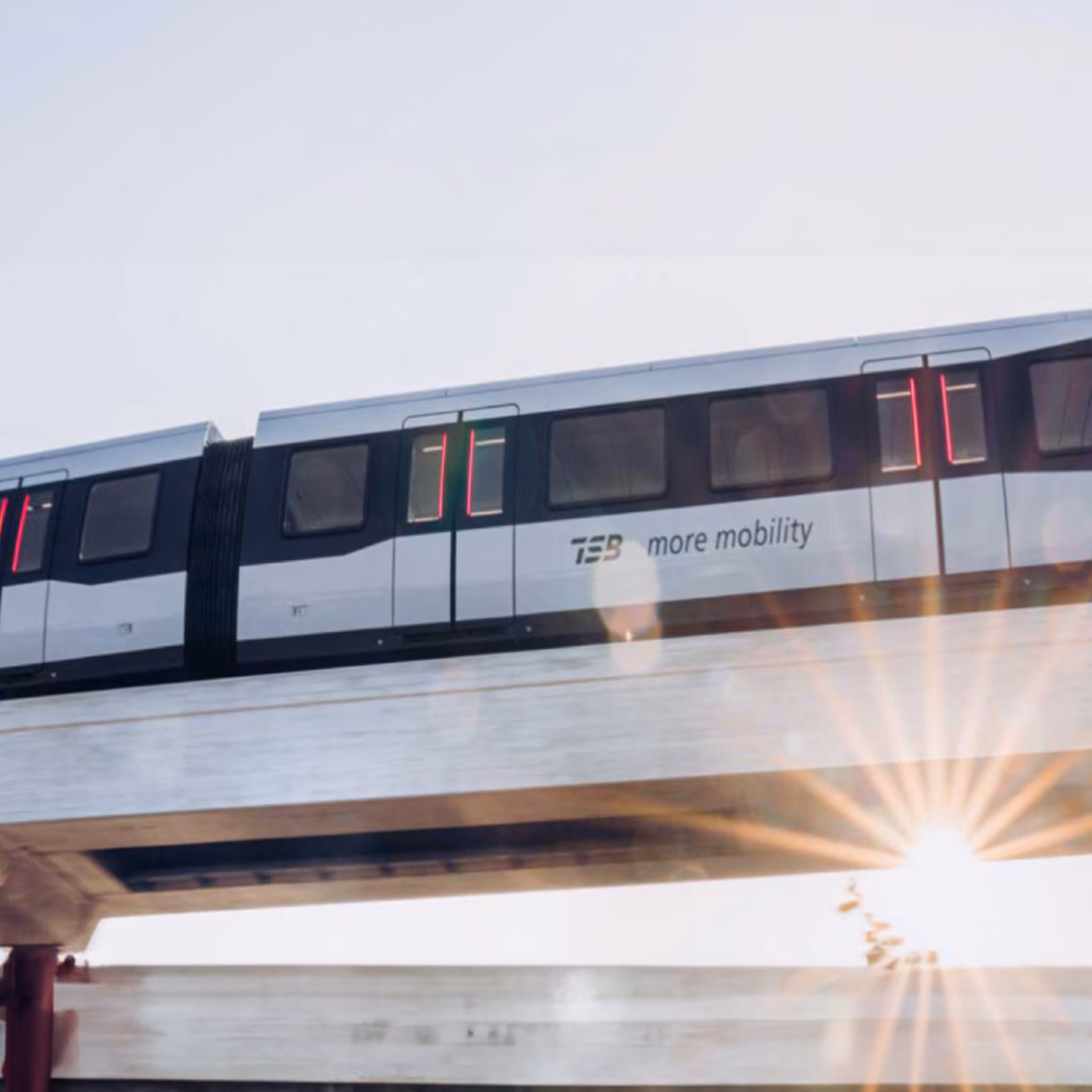 A white TSB maglev train stands on an elevated concrete guideway, the low sun flaring out beneath the beam.
