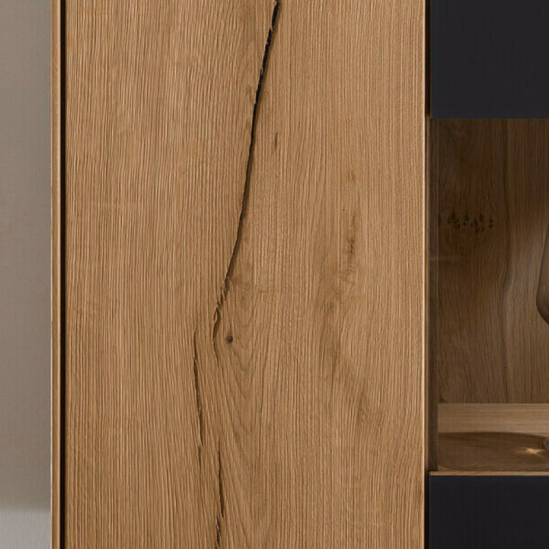 An oak cabinet front with a dark vertical joint running down the grain, next to a lit glass niche holding a wine glass.