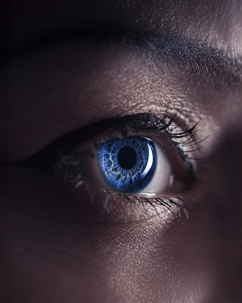 Extreme close-up of one blue eye, the surrounding face in near darkness.