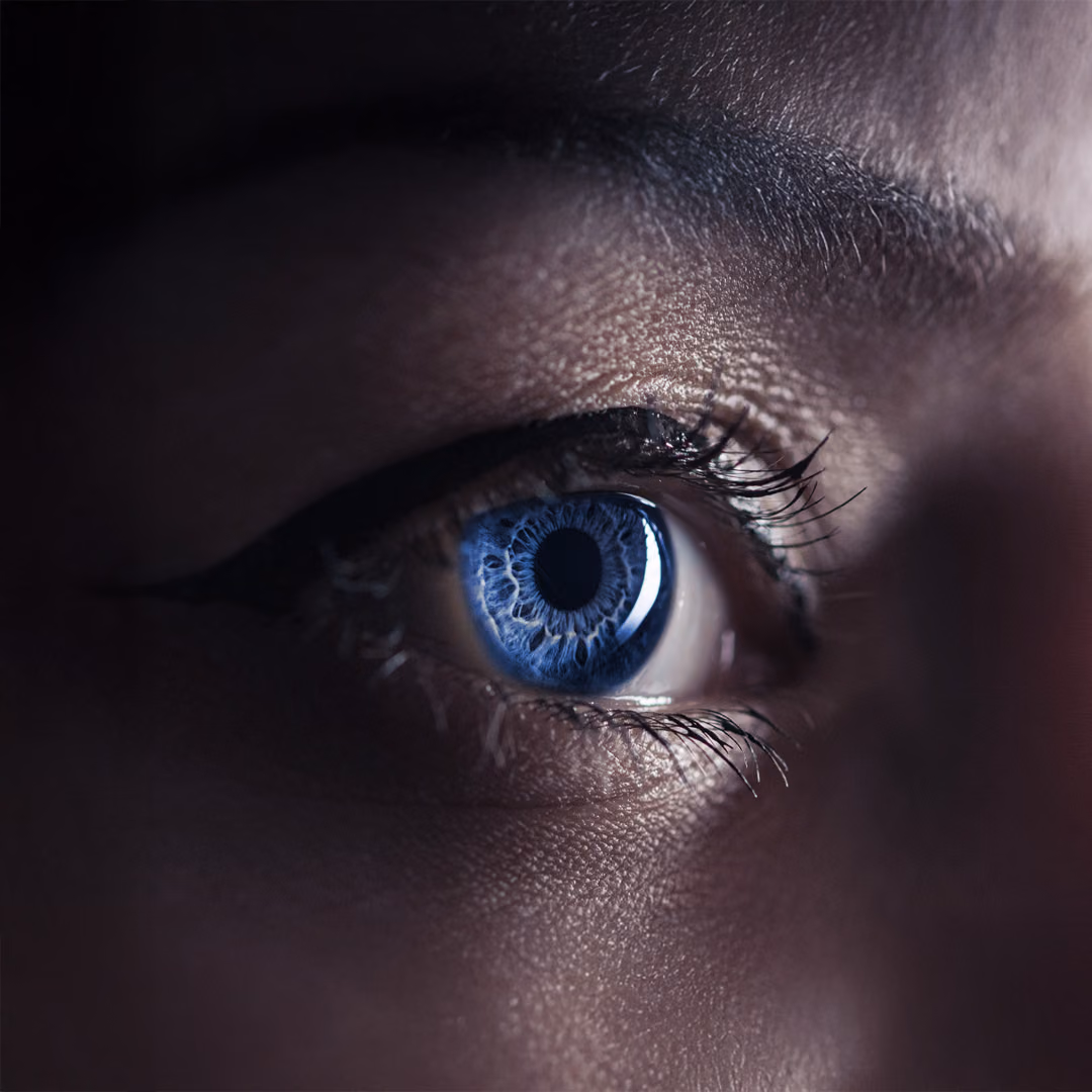 Extreme close-up of one blue eye, the surrounding face in near darkness.