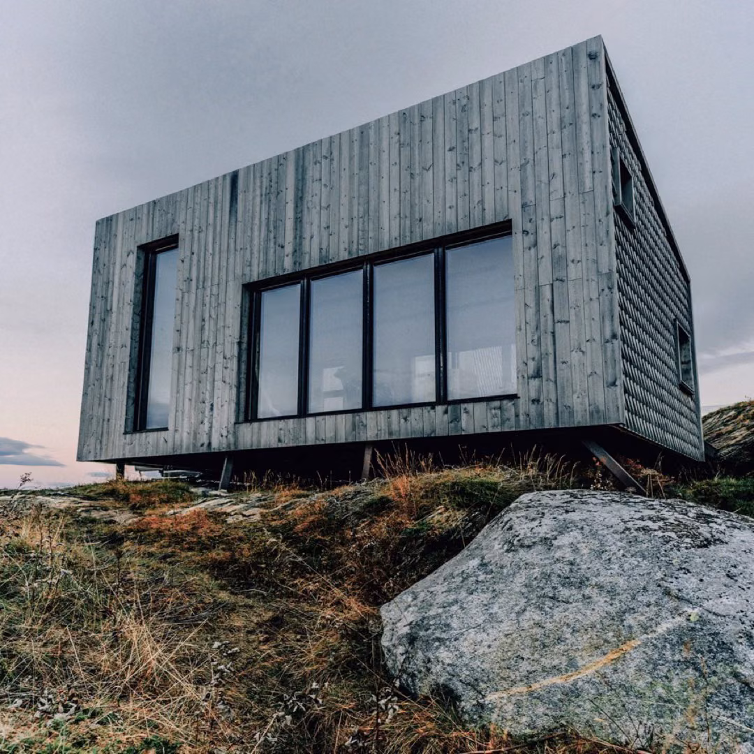 A timber-clad house with large windows on a hillside at dusk.
