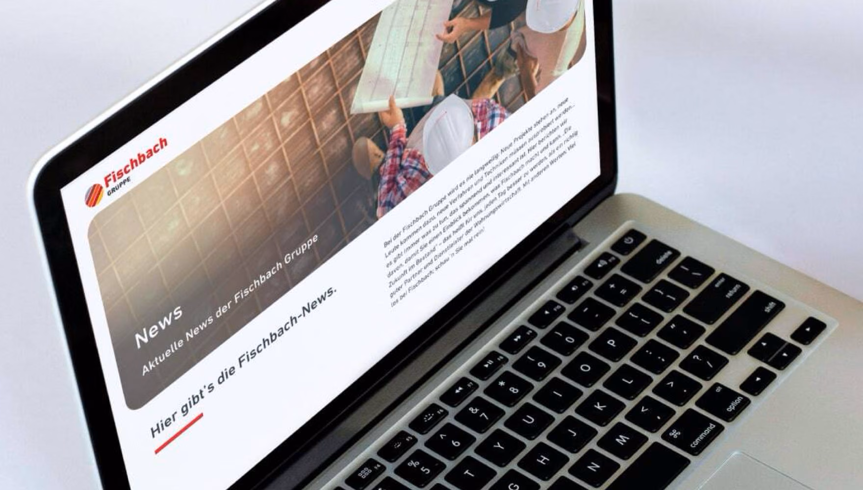 A hand types on a MacBook that shows the Fischbach Gruppe news page.