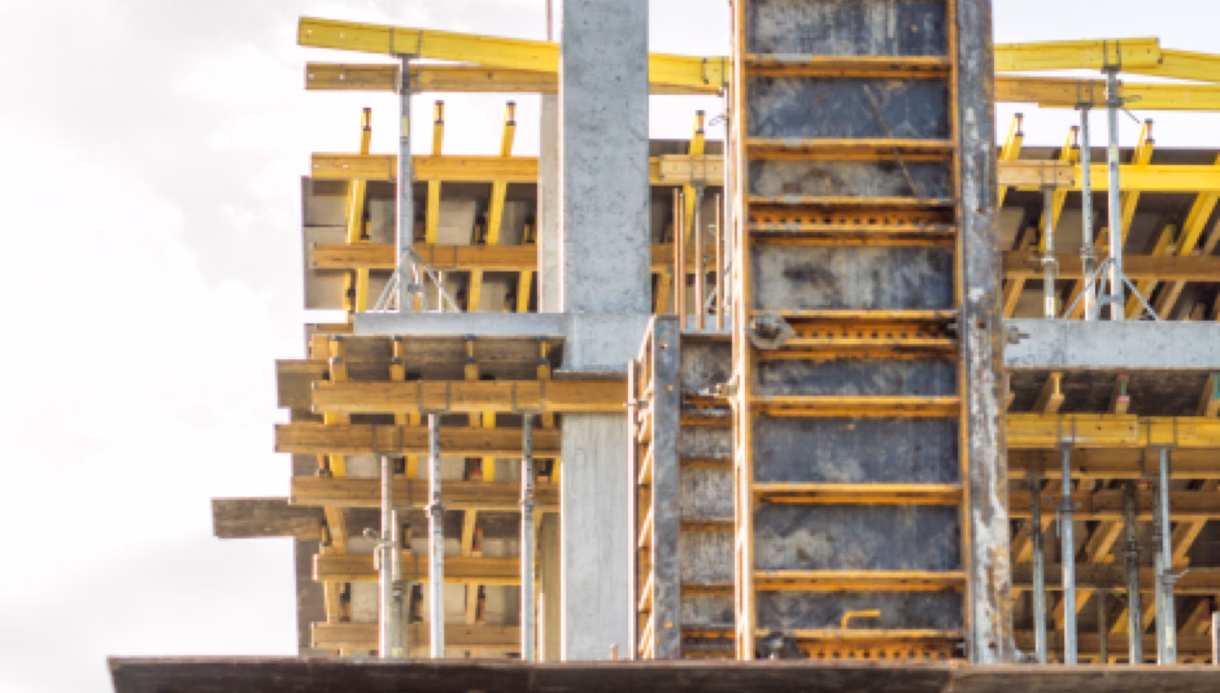 The top storey of a building under construction, timber and yellow beam formwork carrying the slab between bare concrete columns.