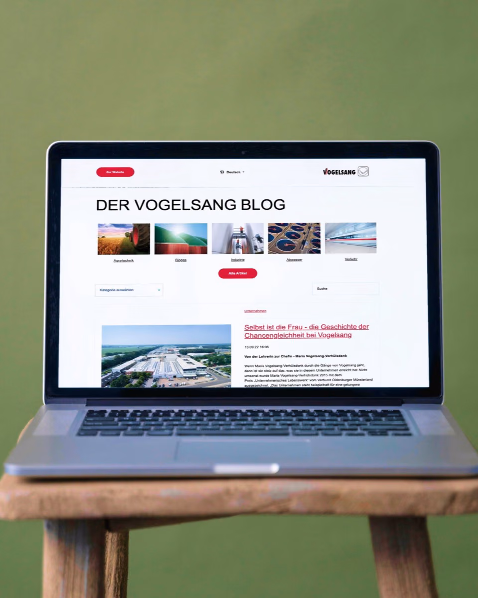 A laptop on a wooden stool shows "Der Vogelsang Blog" with category tiles for agricultural technology, biogas, industry, waste water and transport above the newest article.