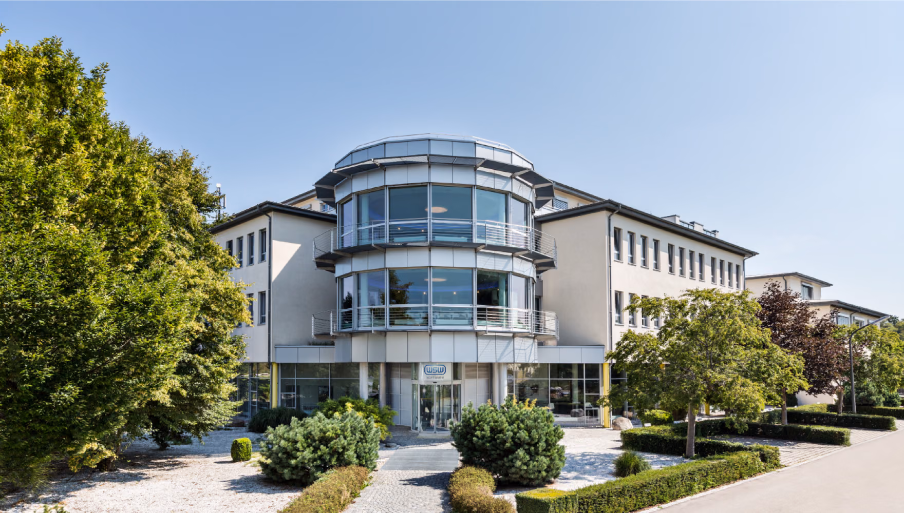 The WSW Software office building, three storeys with a rounded glass stair tower, behind clipped hedges and box balls.