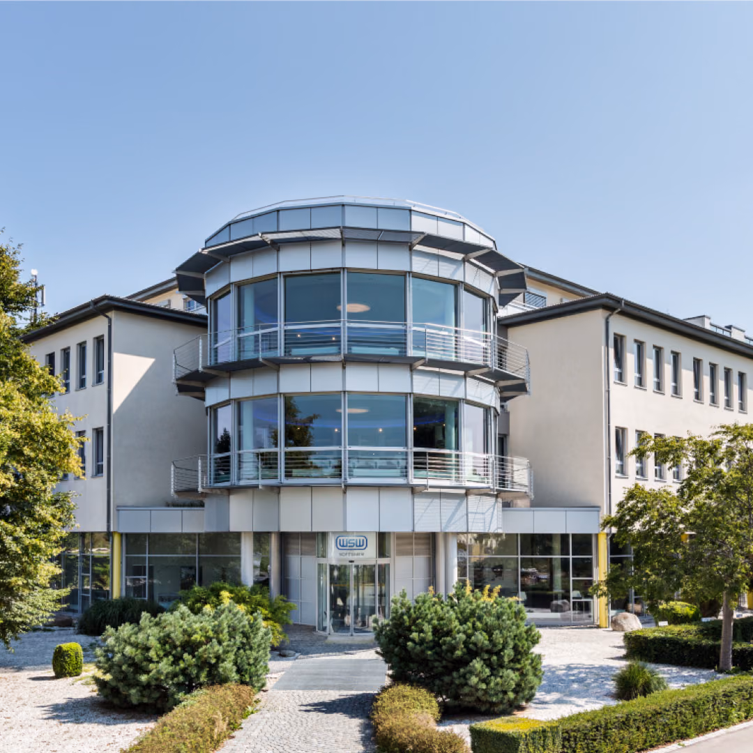 The WSW Software office building, three storeys with a rounded glass stair tower, behind clipped hedges and box balls.