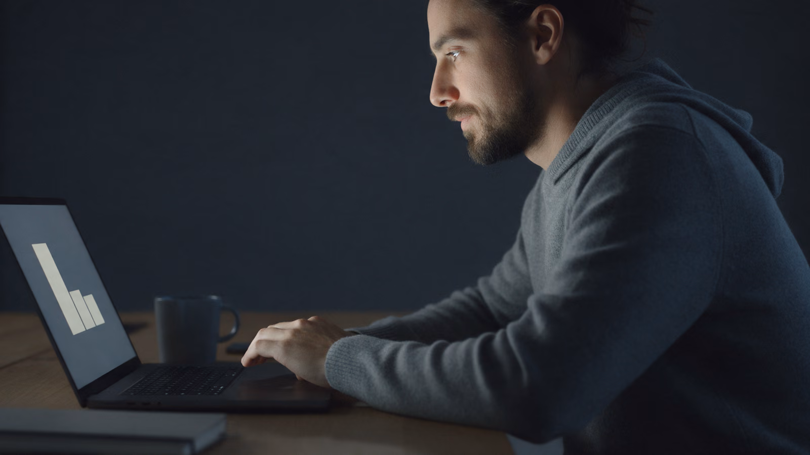 Man reading at a laptop late in the evening, his face lit by the screen.