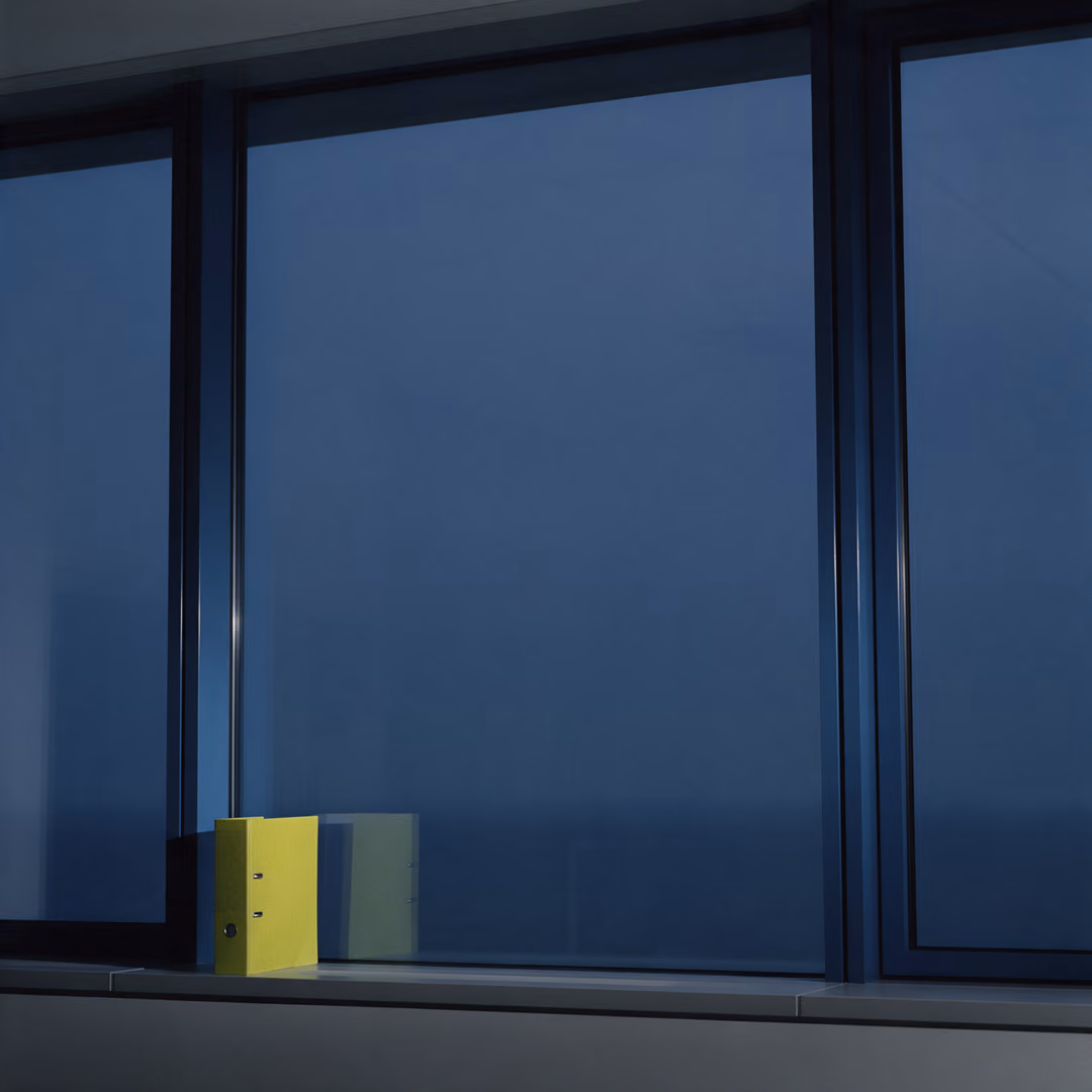 A dark office window wall at dusk with a lime-yellow ring binder standing on the sill.