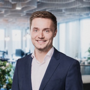 Smiling man in a dark blue suit in a bright office.